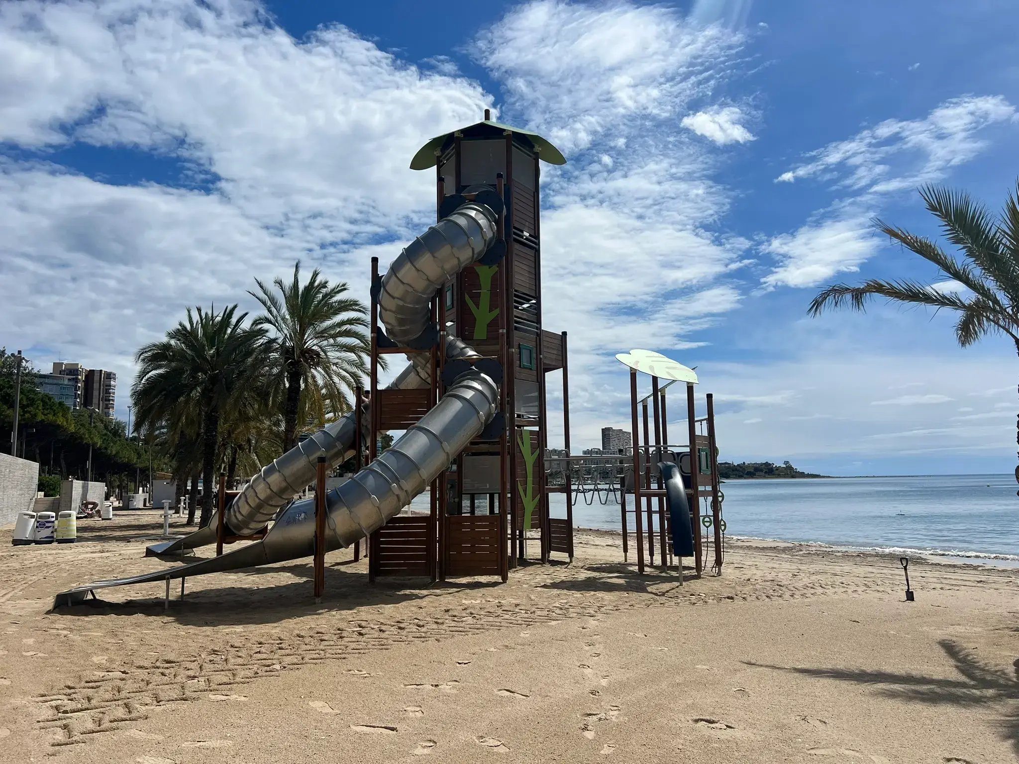 Safe kids' play area at Playa de l'Albufereta with palm trees near the calm Mediterranean shore.
