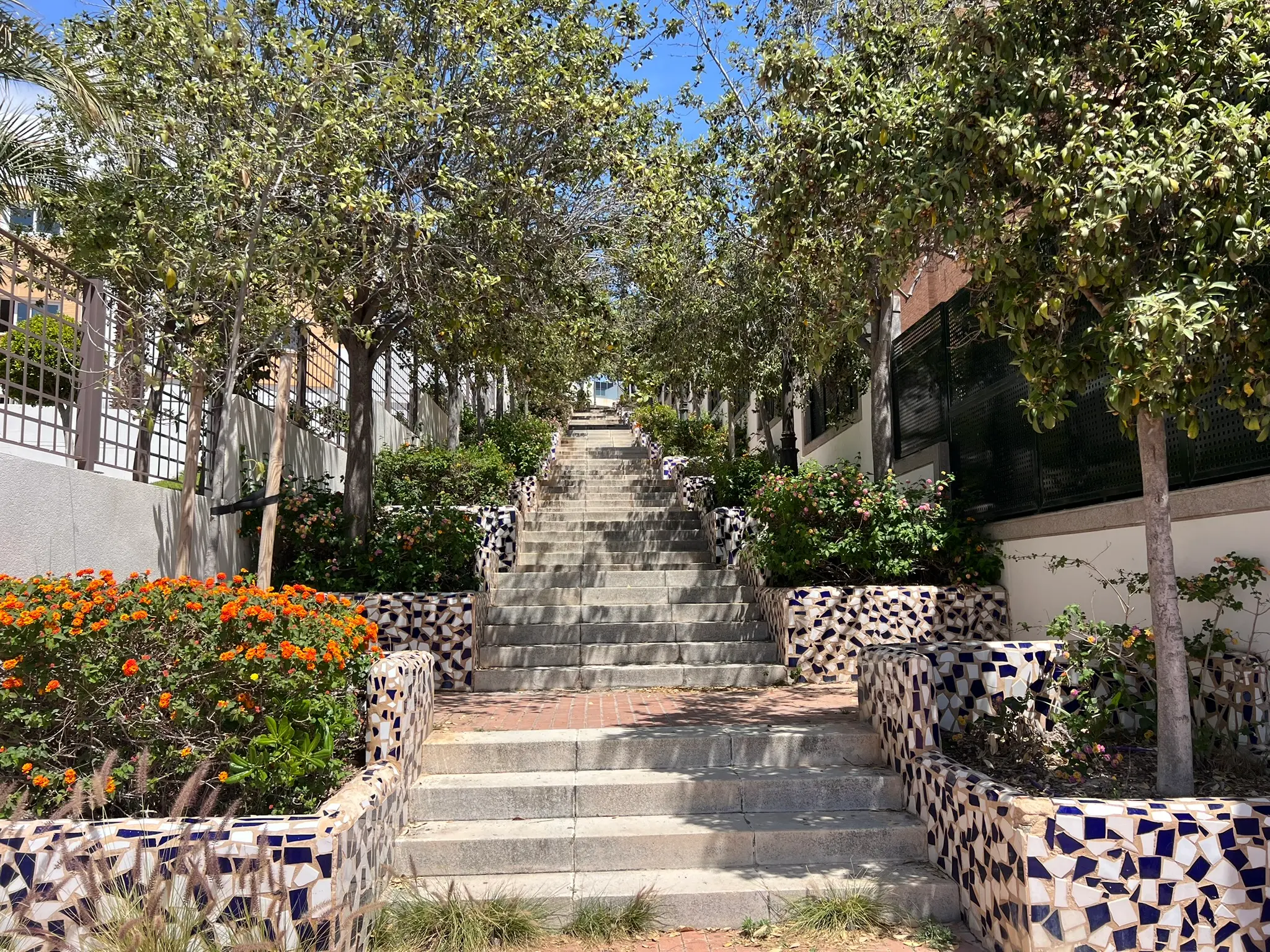 Cala Cantalar Alicante — decorative mosaic tiled staircase leading to Cabo de las Huertas coastal path, surrounded by flowering plants and trees