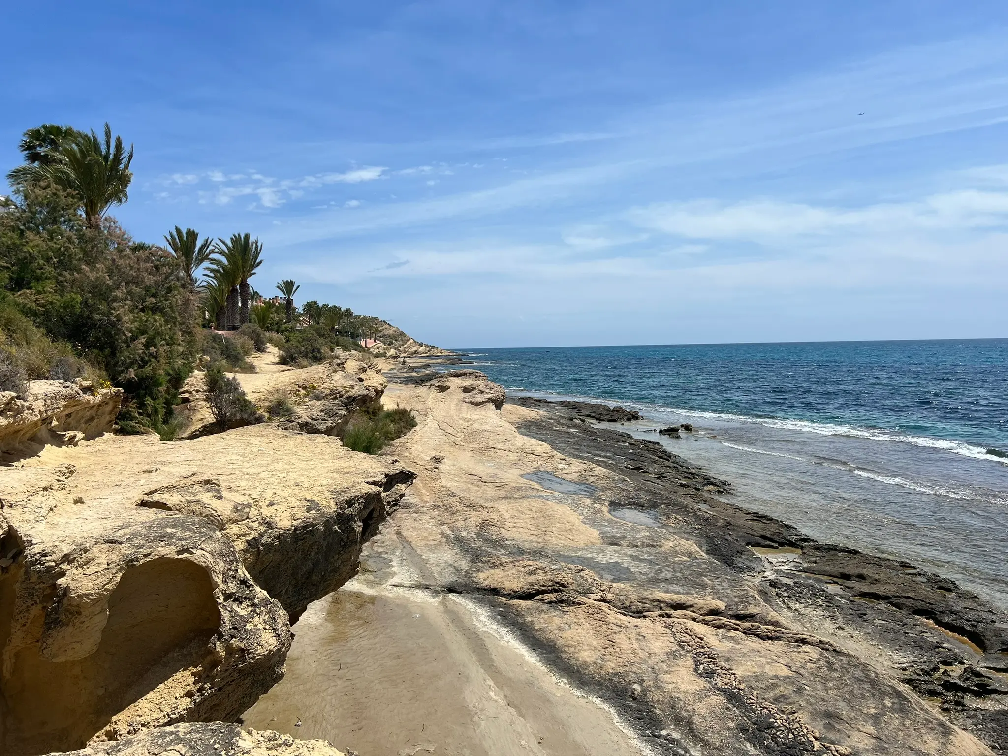 Cala Cantalar Alicante — dramatic golden rock formations along Cabo de las Huertas coastal trail with crystal clear Mediterranean sea and palm trees