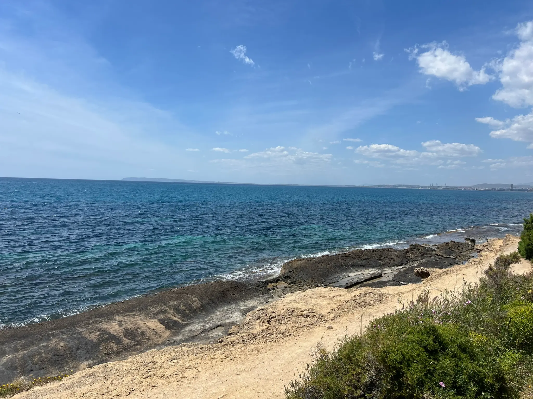 Cala Cantalar Alicante — rocky headland at Cabo de las Huertas with open Mediterranean sea views and Alicante port visible in the distance, coastal hiking trail