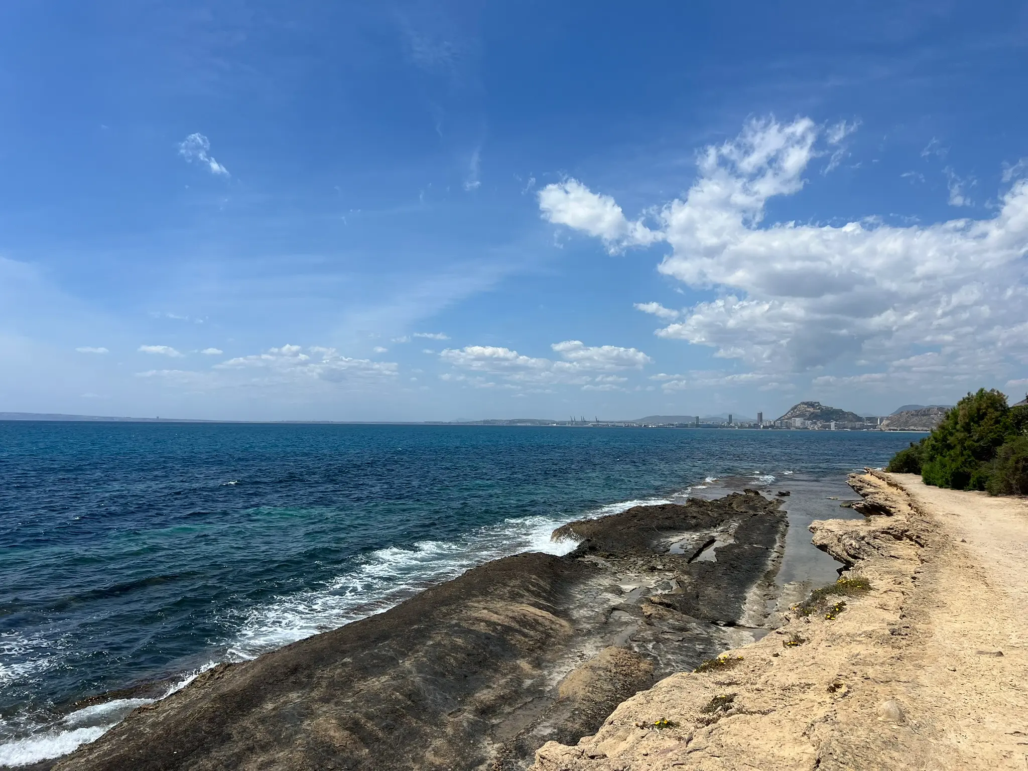 Cala Cantalar Alicante — coastal walking path along Cabo de las Huertas rocks with panoramic views of Alicante city and Santa Barbara Castle in the distance