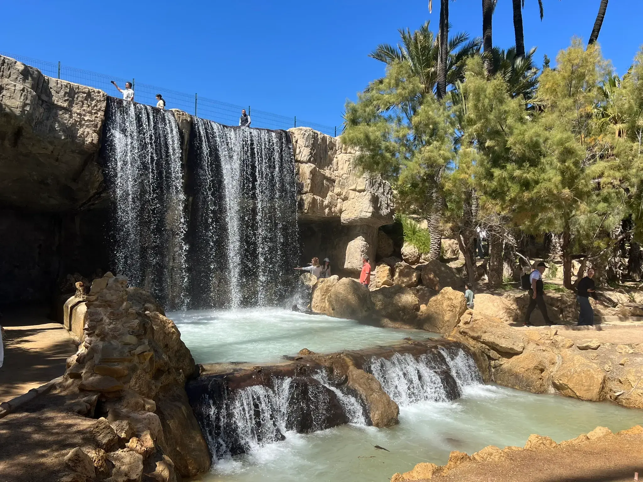 Ornamental waterfall at El Palmeral Park in Alicante — cascading water feature framed by palms and tropical greenery.
