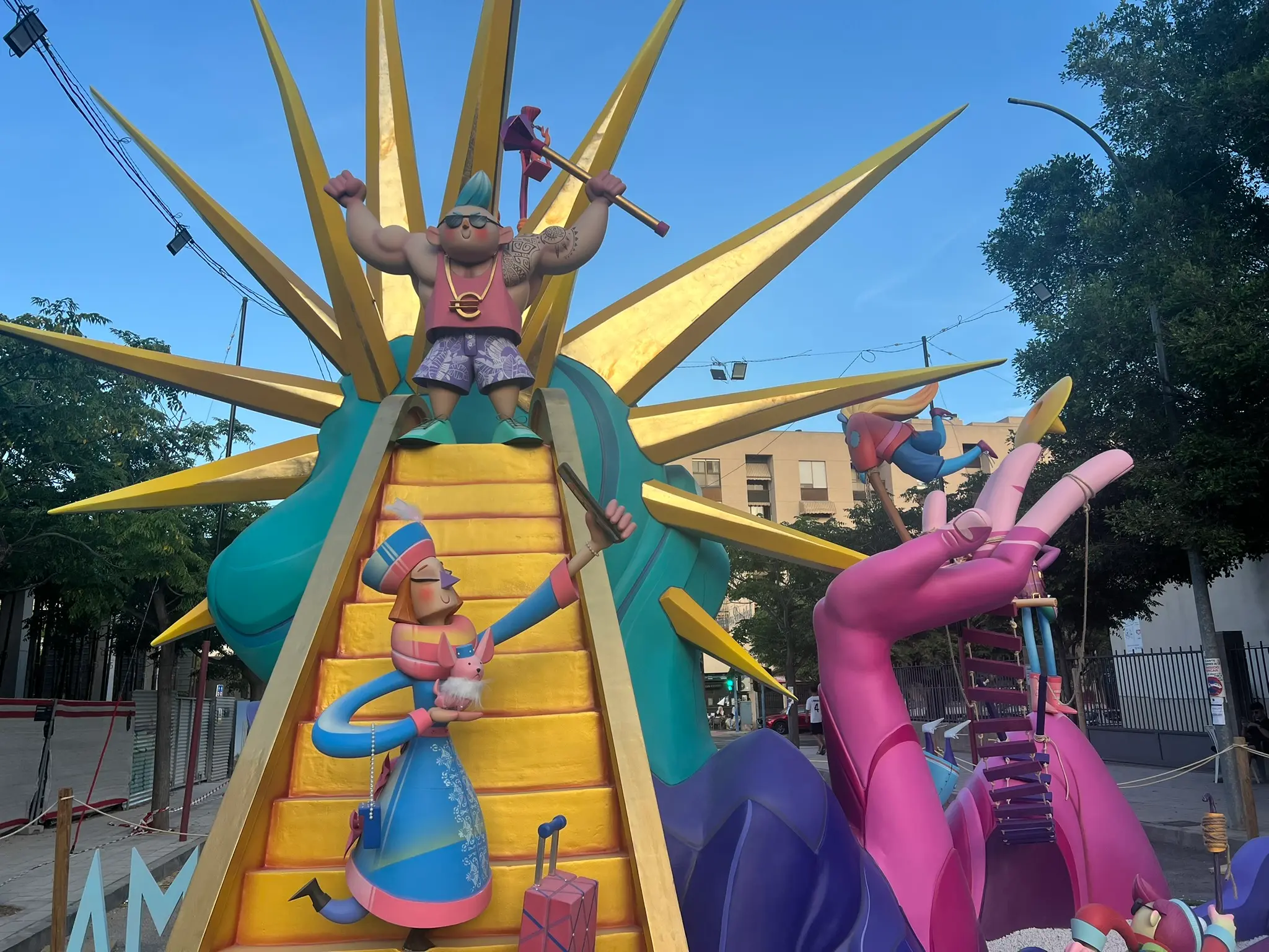 Close-up of a Hogueras monument featuring a muscular bodybuilder figure on a golden staircase and a girl taking a selfie at the bottom