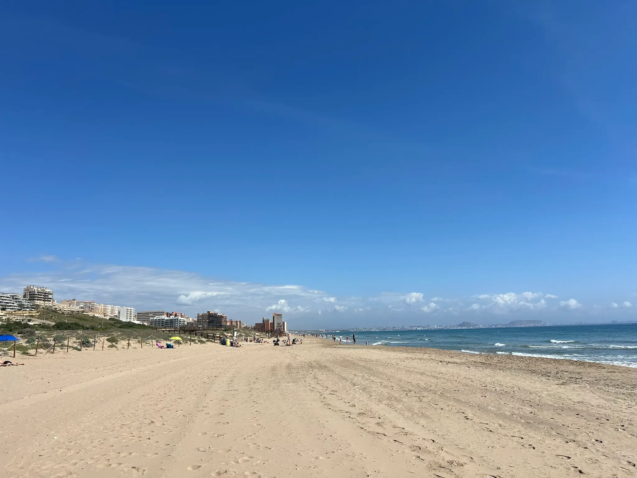A breathtaking wide-angle view of the pristine Platja del Carabassí beach in Alicante, featuring a sprawling wooden boardwalk meandering through a protected sand dune ecosystem.