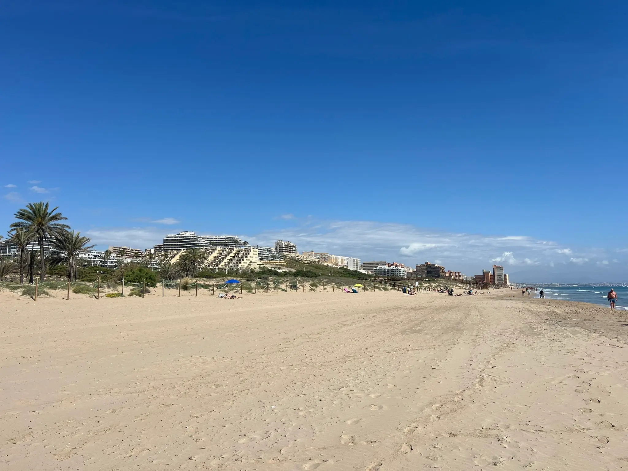 A picturesque view of the golden sands and gentle waves at Platja del Carabassí beach under a bright blue sky.