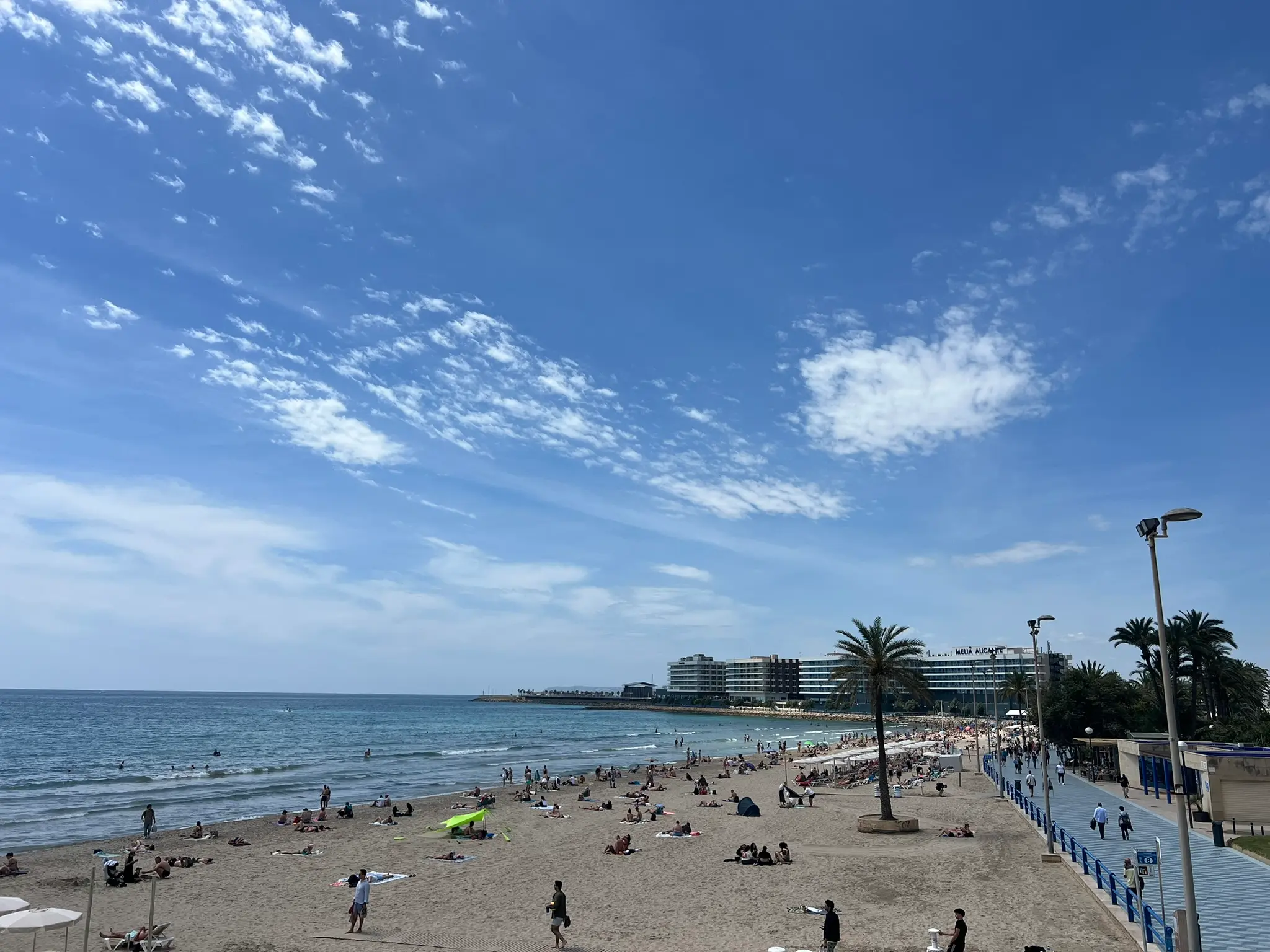 Playa del Postiguet Alicante — busy city centre beach with sunbathers, palm-lined promenade and Melia Alicante hotel in the background, most popular beach in Alicante