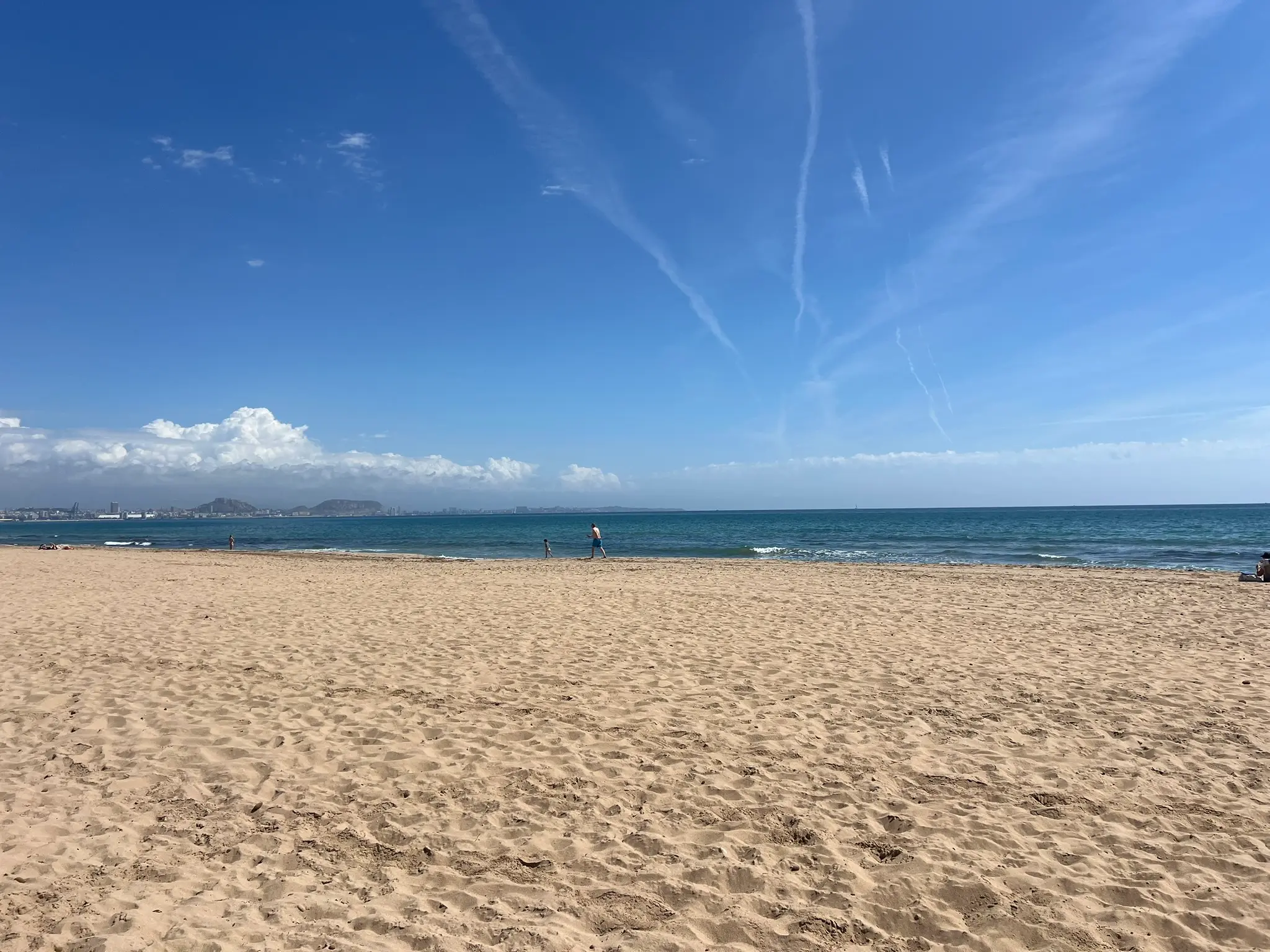 Playa del Saladar Alicante — wide golden sand beach with family at the waterline and Santa Barbara Castle visible in the distance