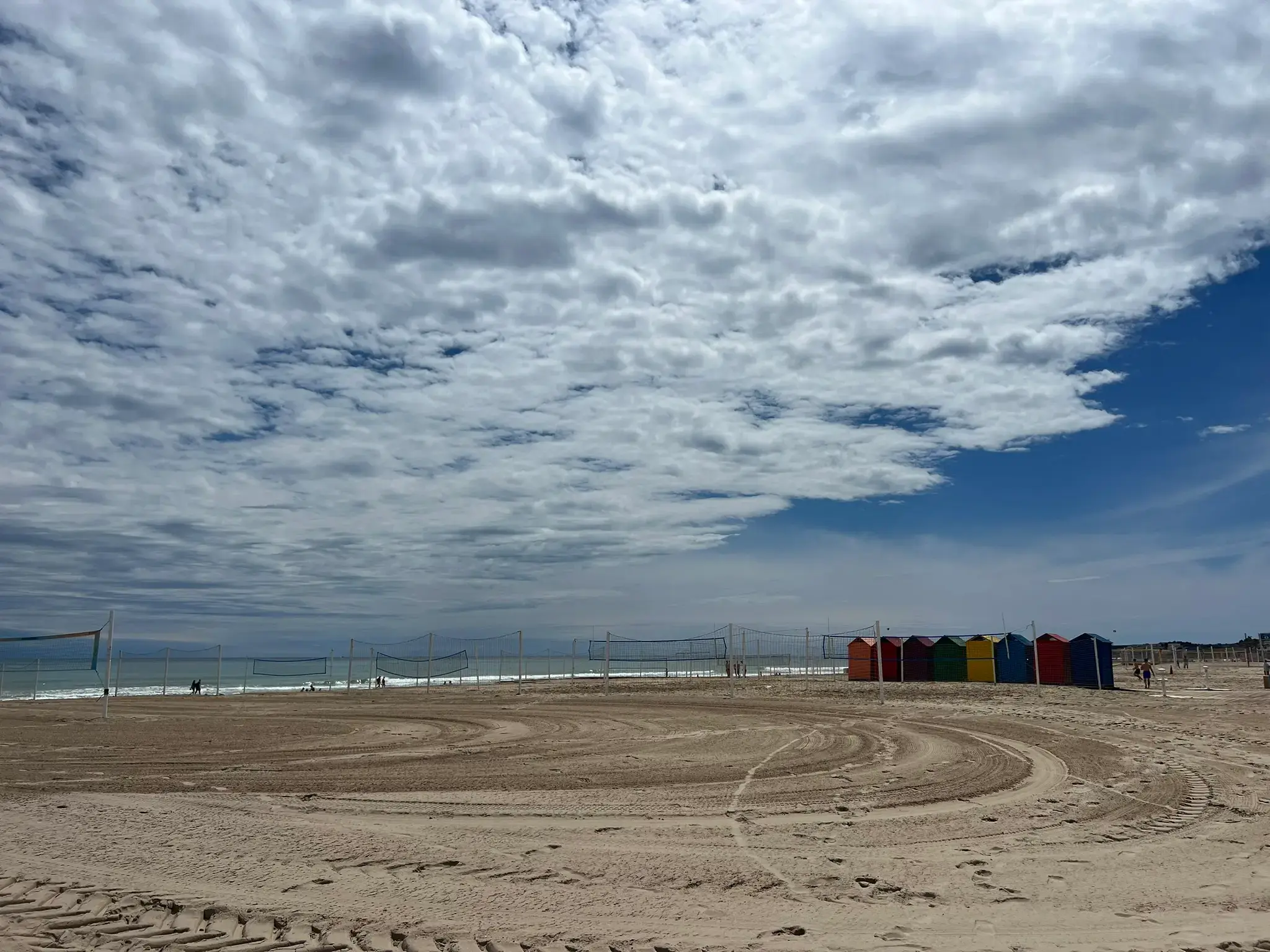 Playa de San Juan Alicante — beach volleyball courts and colourful wooden beach huts on wide sandy beach with Mediterranean sea in the background.