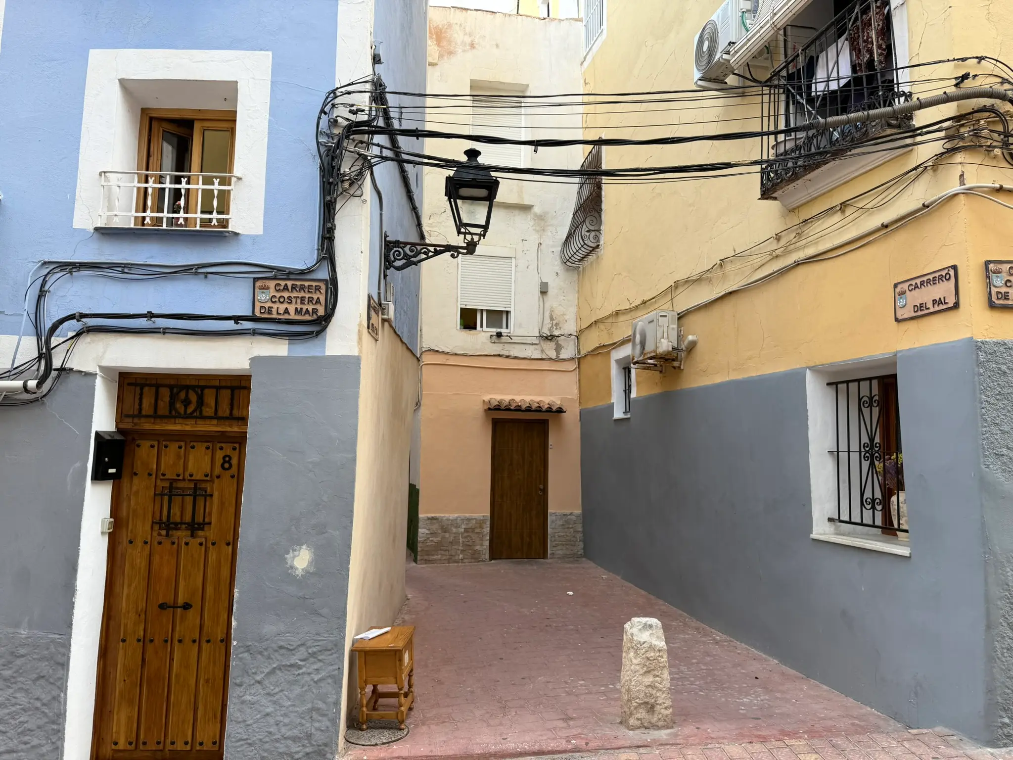 Street corner with signs for Carrer Costera de la Mar and Carrero del Pal in Villajoyosa — blue and yellow houses, wooden door, vintage lamp