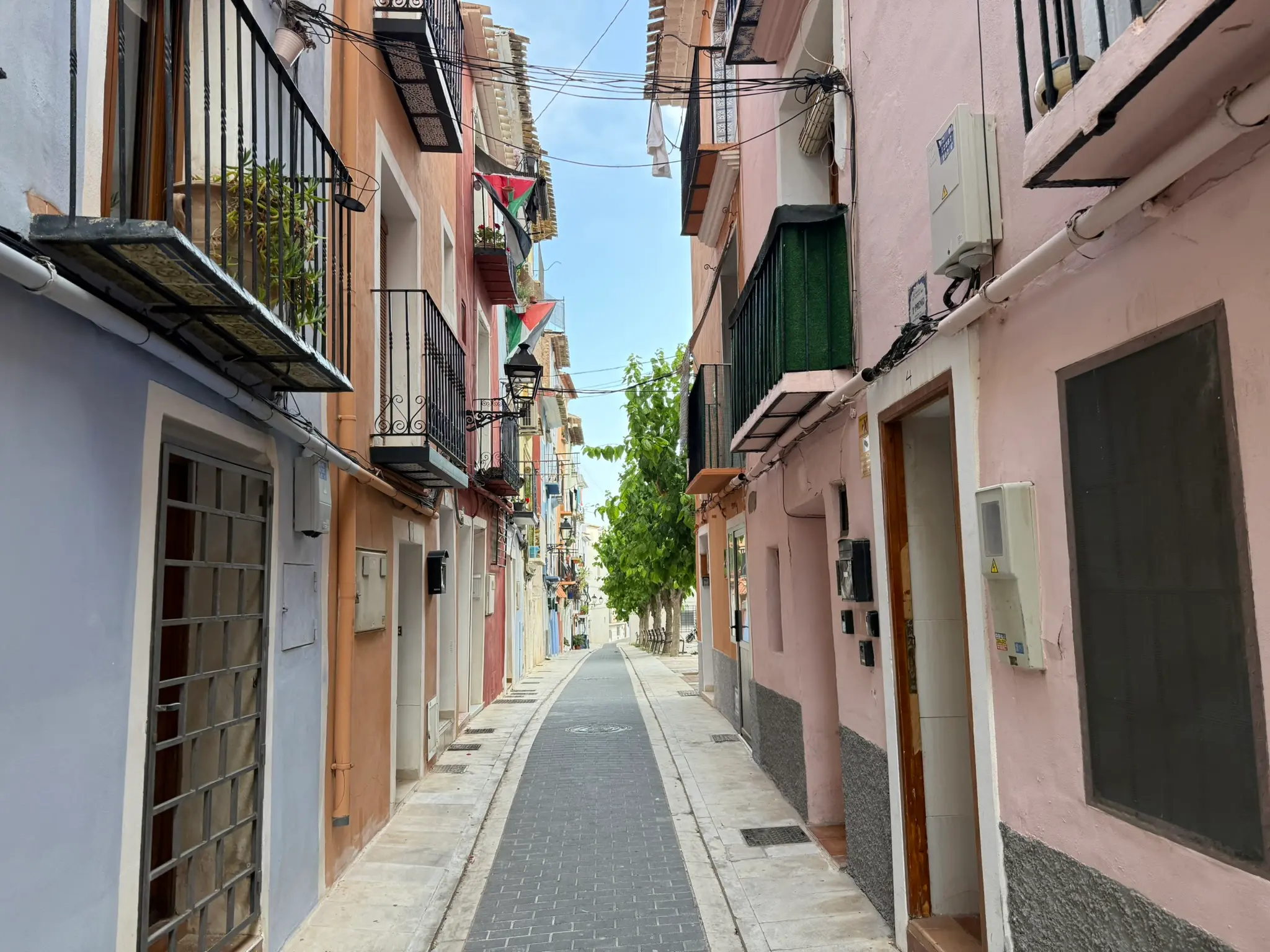 Perspective view down historic Carrer Major in Villajoyosa — narrow paved street with lavender, orange, and pink traditional houses with iron balconies