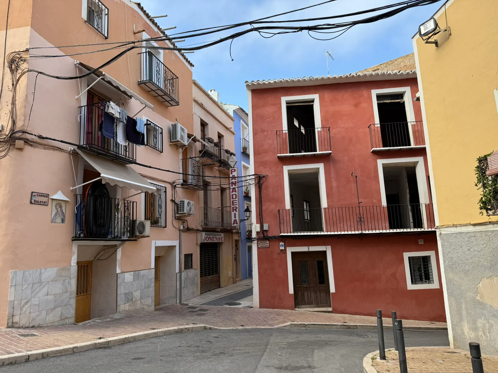 Old town intersection of Carrer Soletat in Villajoyosa — historic pink and red buildings, traditional bakery sign, drying laundry, religious tile icon