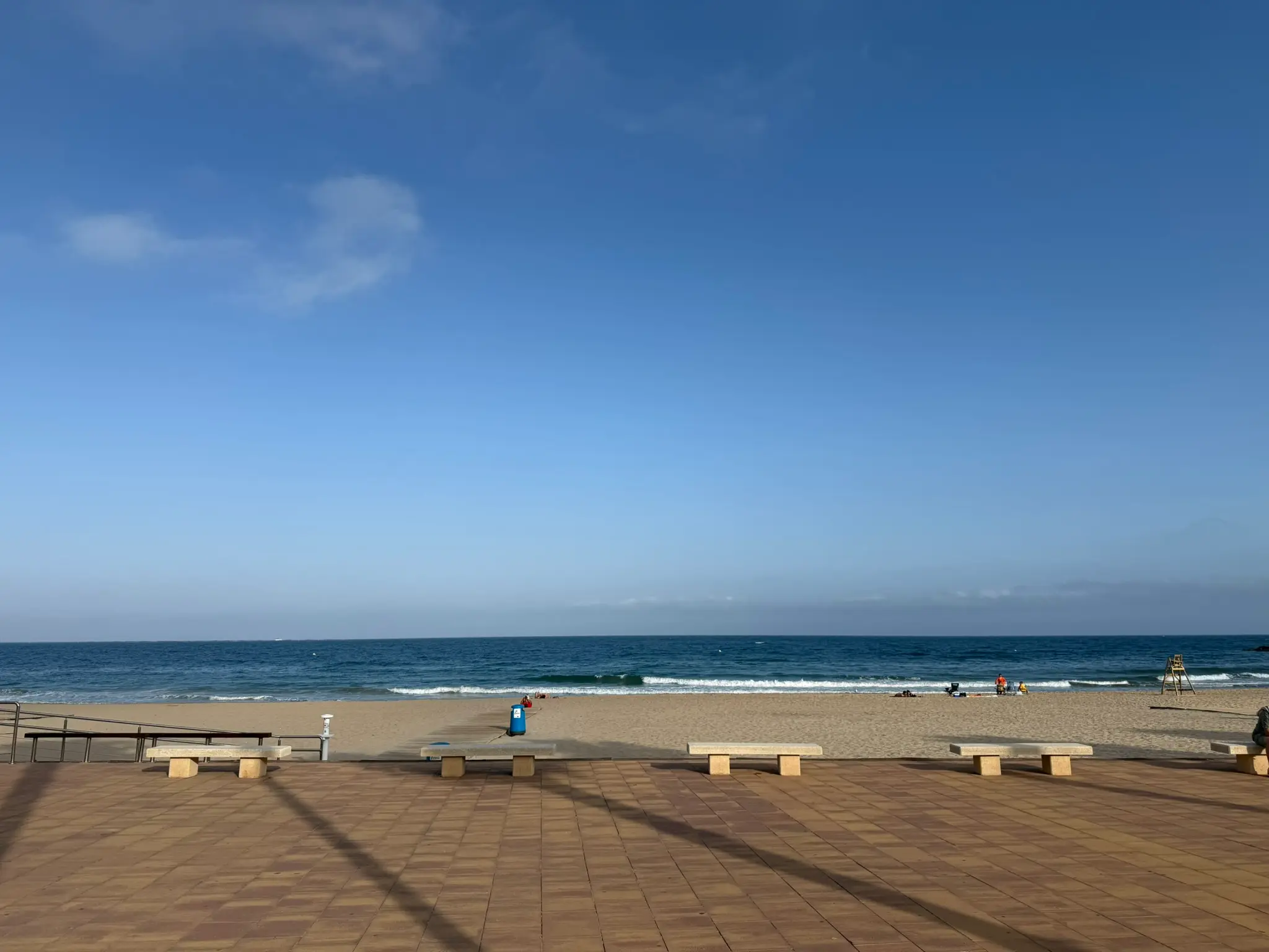Scenic view of sandy Playa Centro beach in Villajoyosa looking out at calm blue Mediterranean — stone public benches on promenade under bright sunny sky