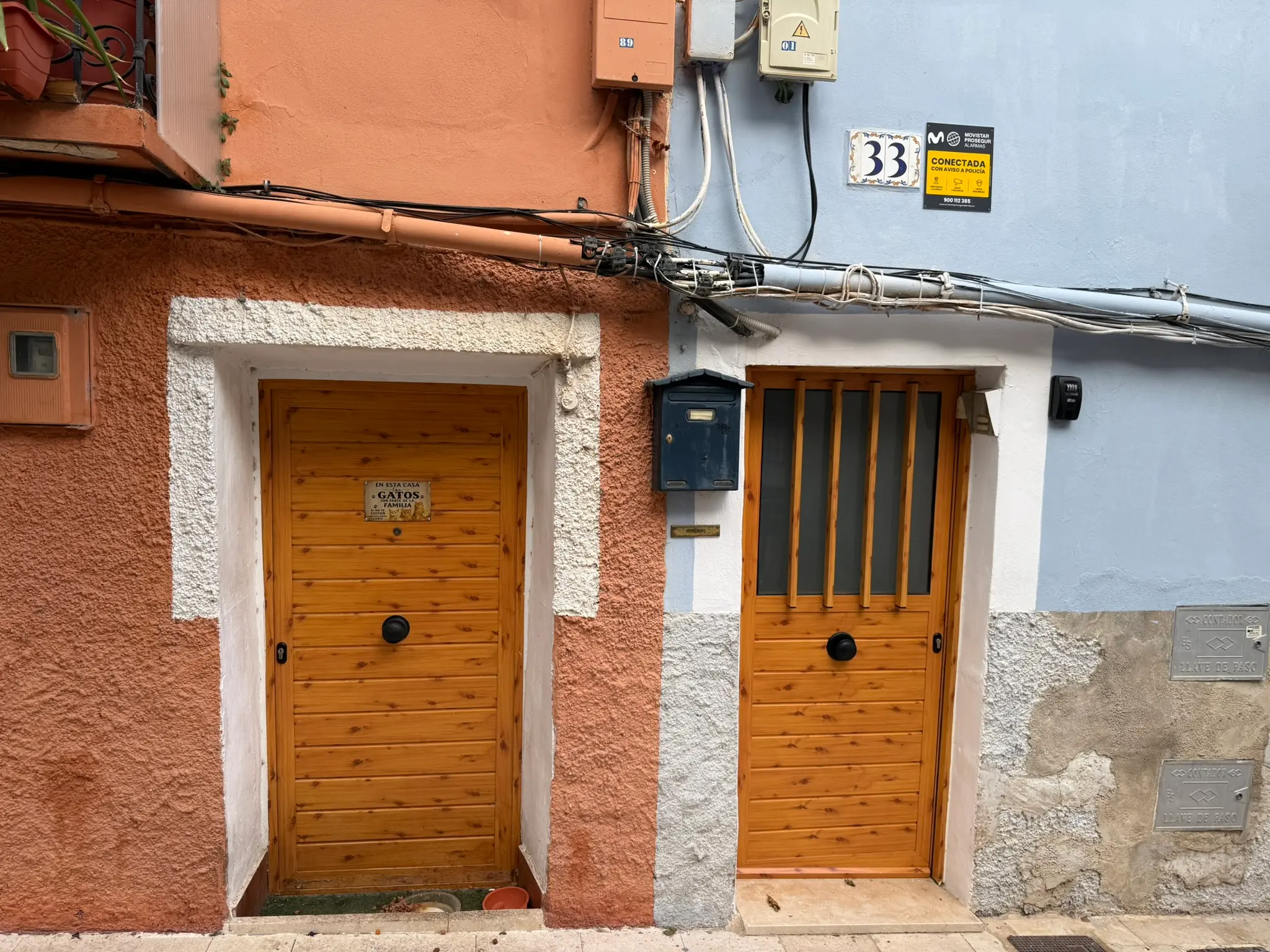 Traditional residential entrance of house 33 in Villajoyosa — contrasting orange and light blue walls, matching wood doors, mailbox, security sign, decorative Spanish tile about cats