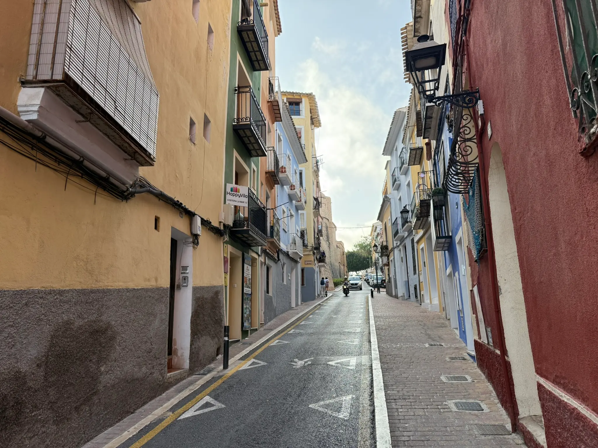 A narrow street on Costera la Mar in Villajoyosa — brightly painted yellow, green, blue, and red houses with balconies