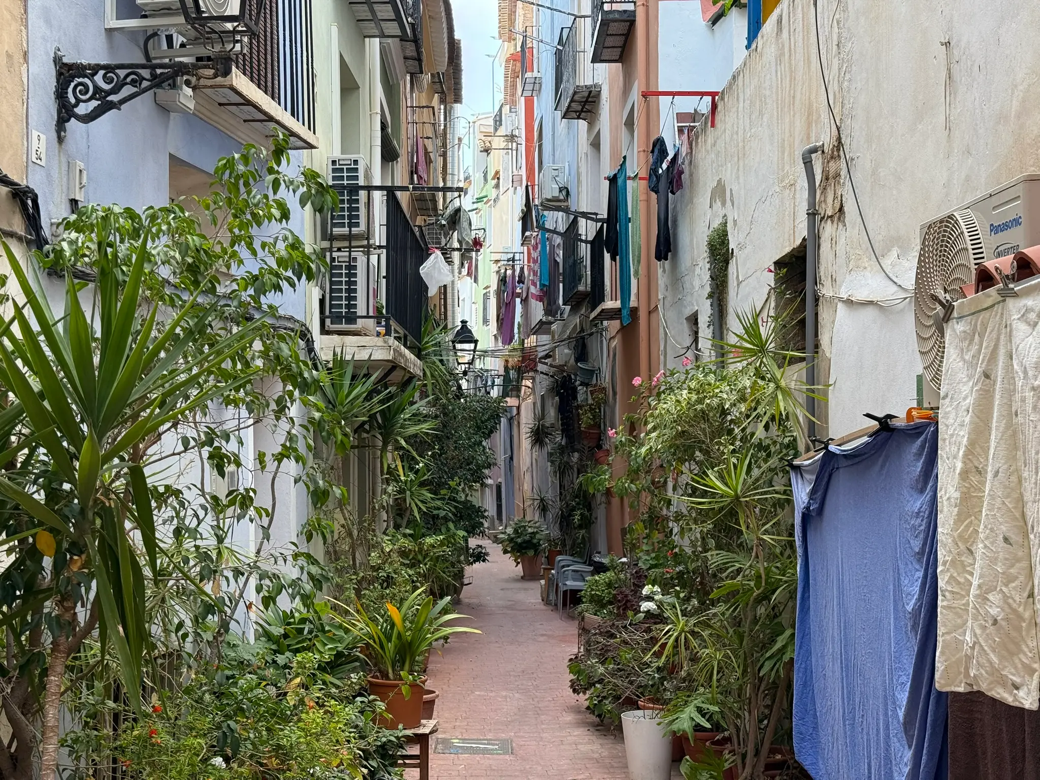 Narrow atmospheric residential alley in Villajoyosa old town — brick-paved path with potted plants and laundry hanging on clotheslines