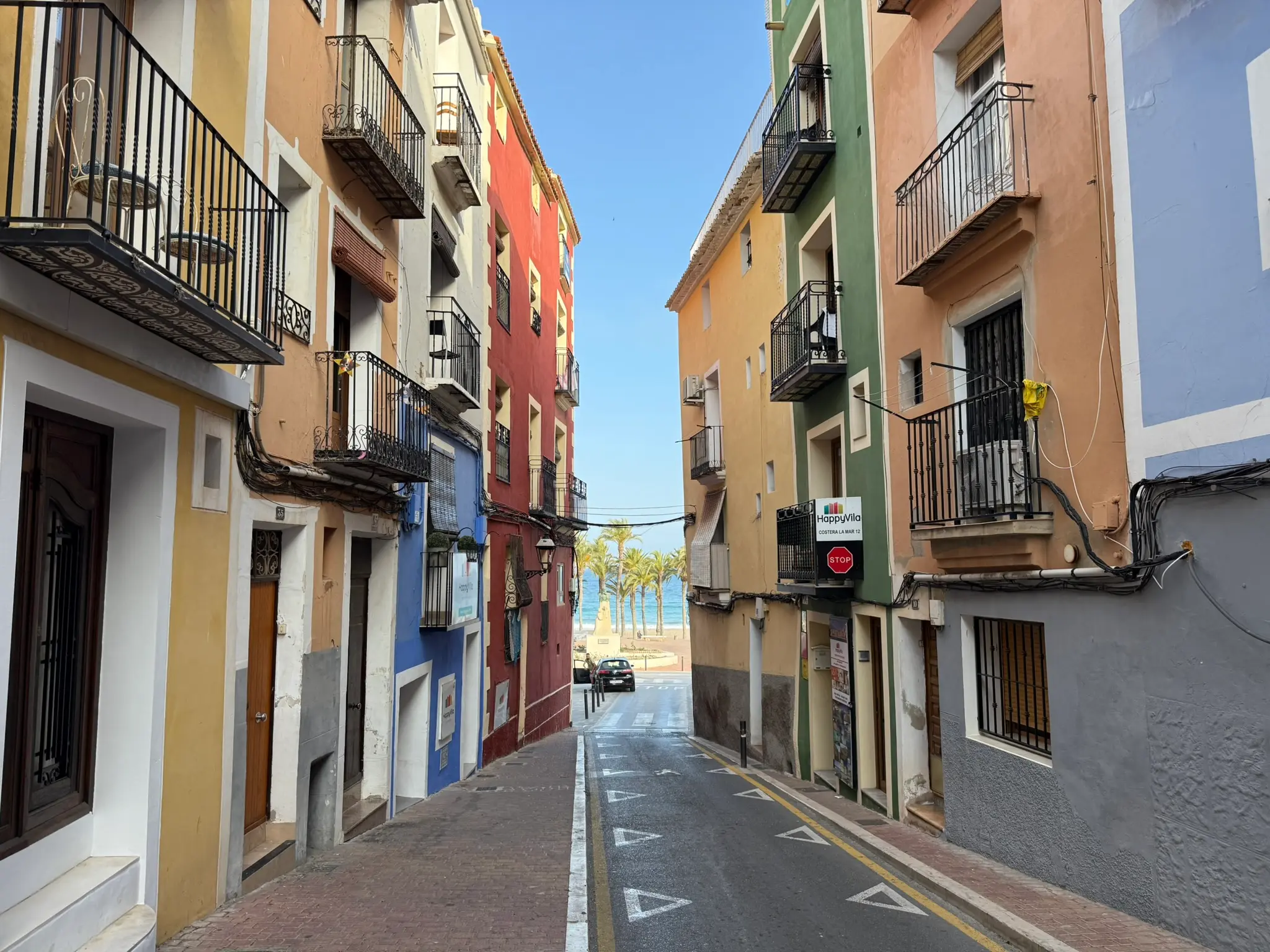 Downhill view of Costera la Mar in Villajoyosa — colourful buildings leading to the beach with palms and sea in distance