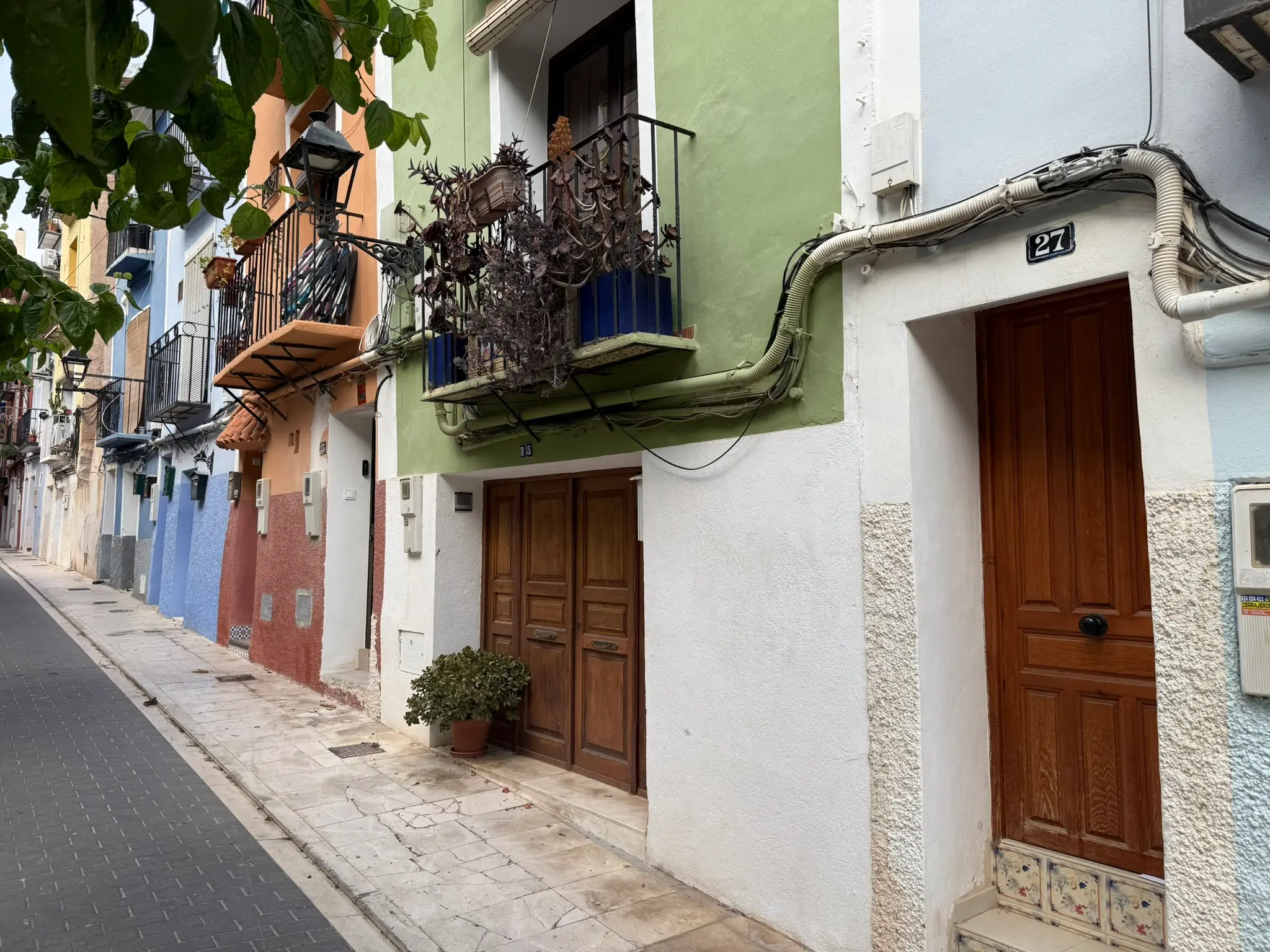 Row of traditional colourful houses numbered 25 and 27 in Villajoyosa — white, green, and terracotta facades with rustic wooden doors and vintage lamp