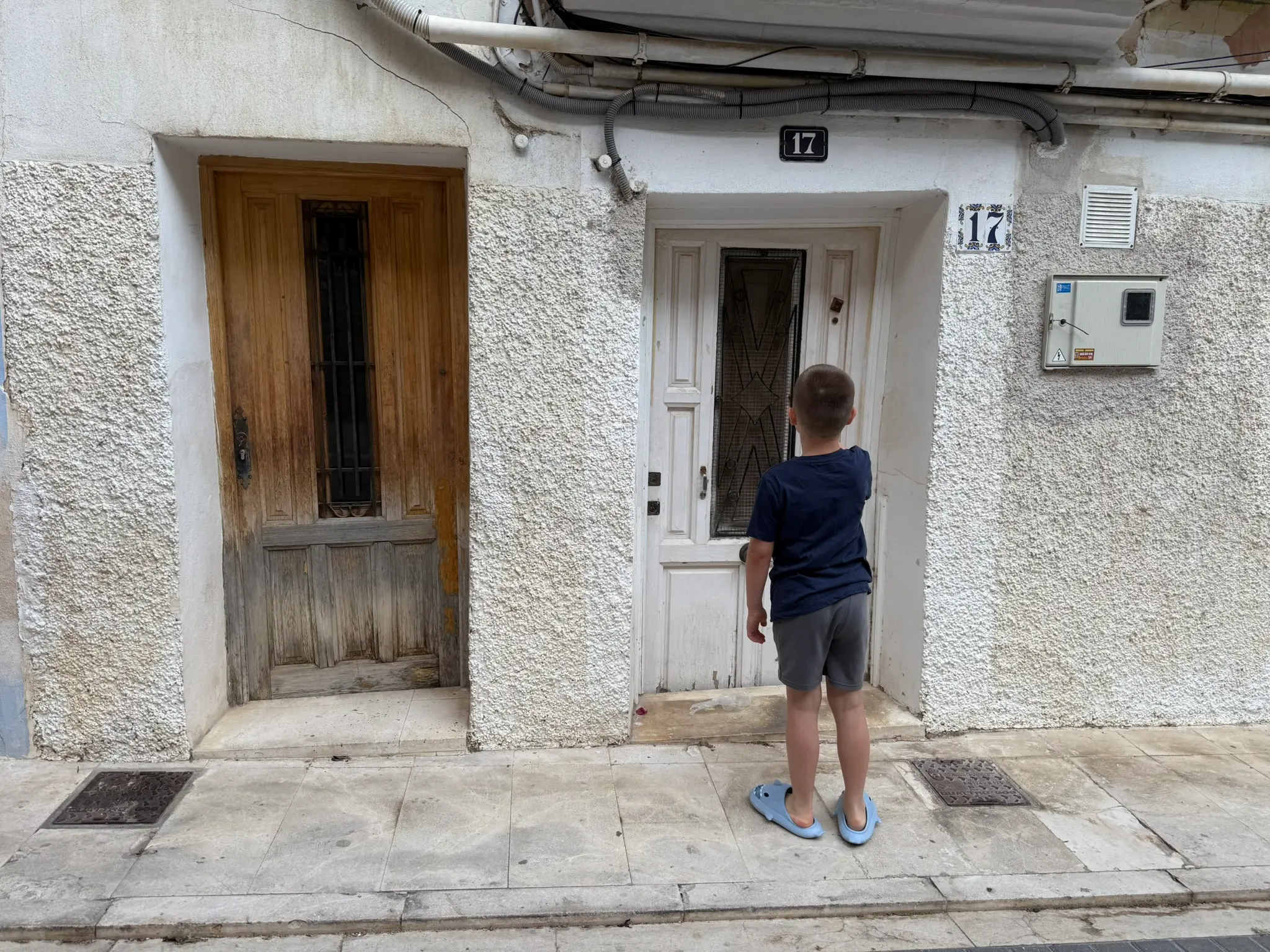 Child viewed from back standing in Villajoyosa old town looking at traditional wooden doors on whitewashed facade numbered 17