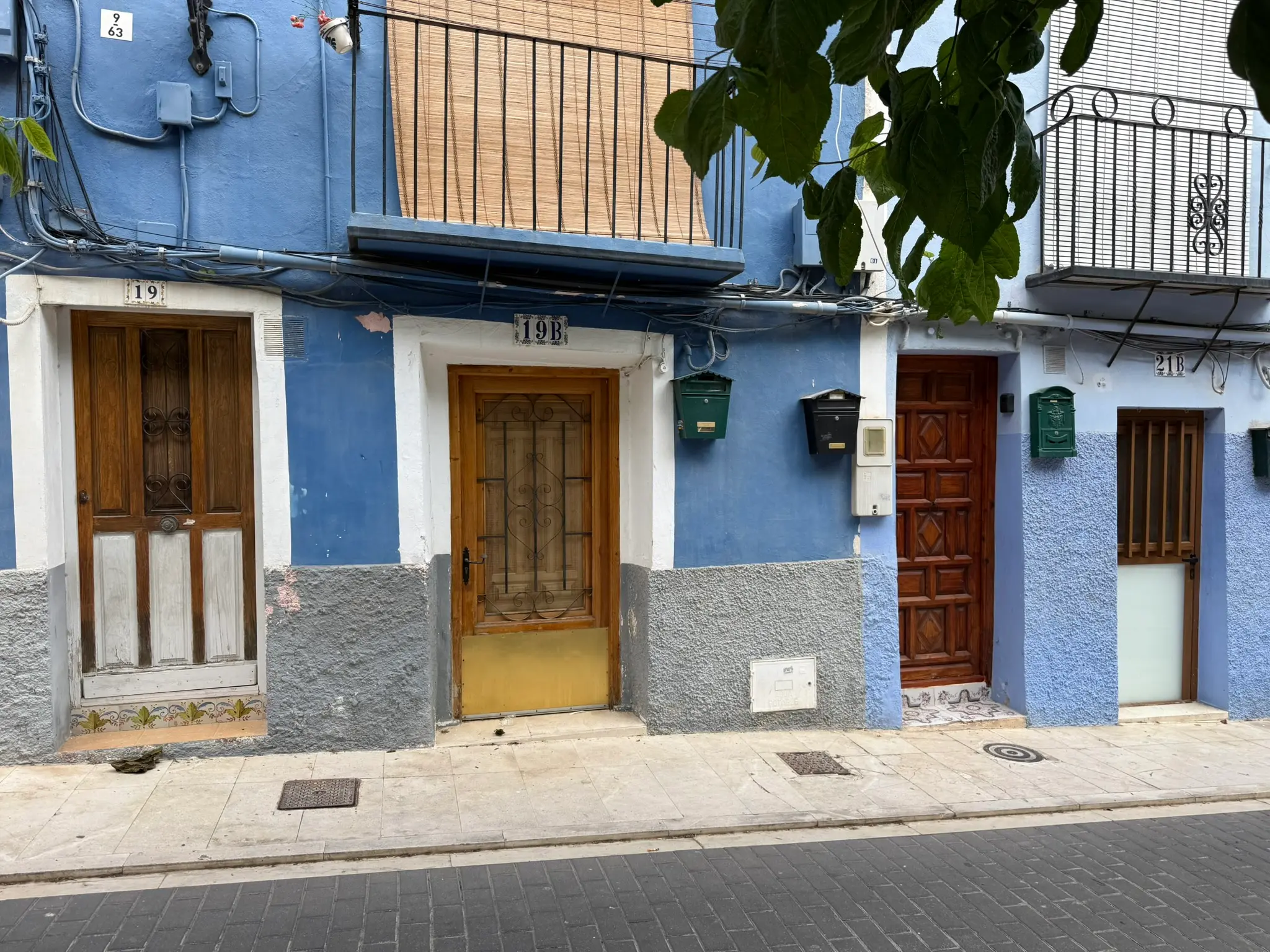 Traditional brightly painted blue houses numbered 19, 19B, and 21B in Villajoyosa — wooden entrance doors, mailboxes, balconies with iron railings